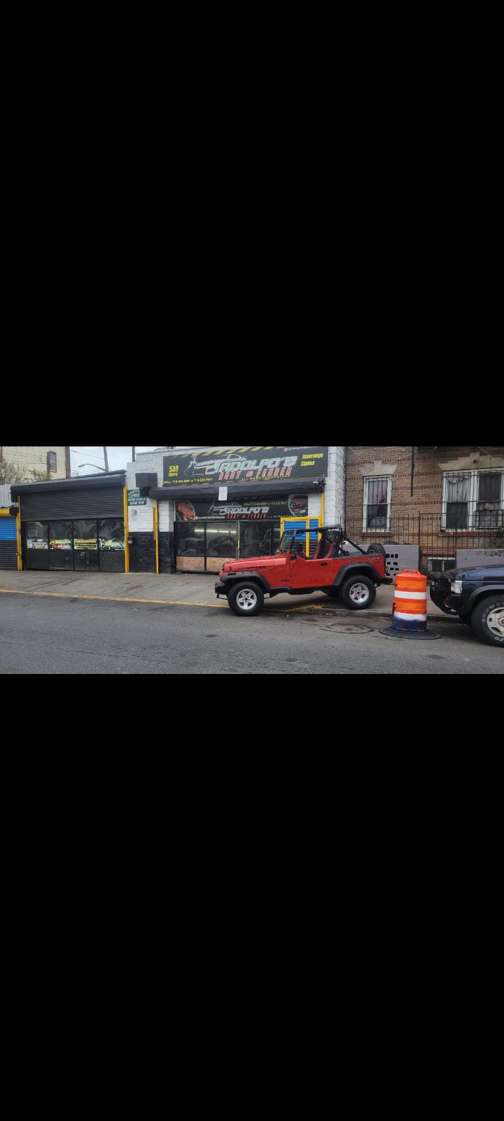 Adolfo's Auto Body storefront on Liberty Avenue with customer vehicles