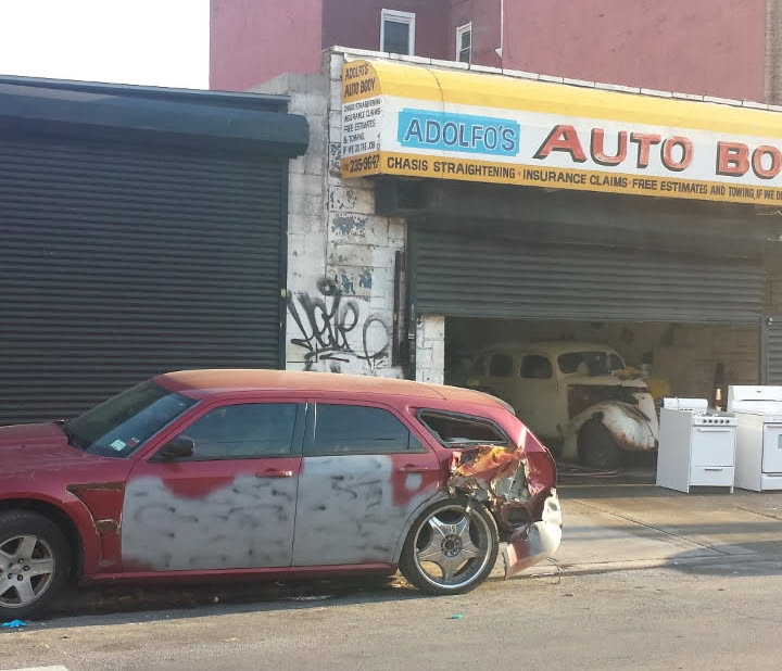 Red station wagon with severe rear-quarter collision damage outside Adolfo's Auto Body