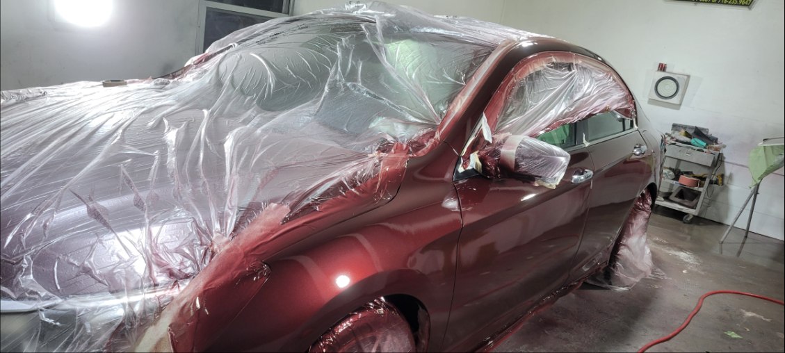 Red sedan fully masked with freshly refinished body panels inside the paint shop